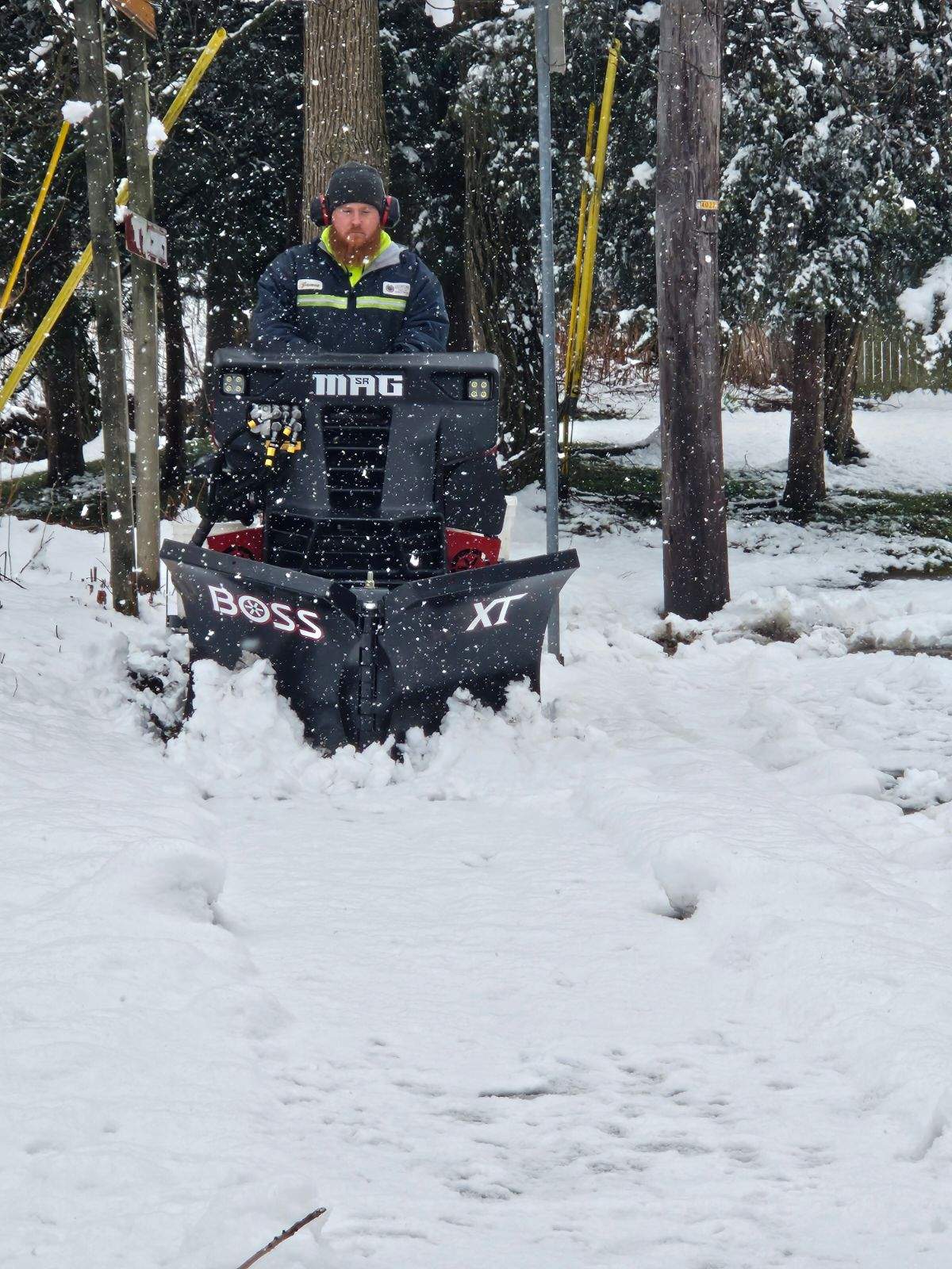 Worker in winter gear in a black BOSS XT snowplow clearing snow among trees.